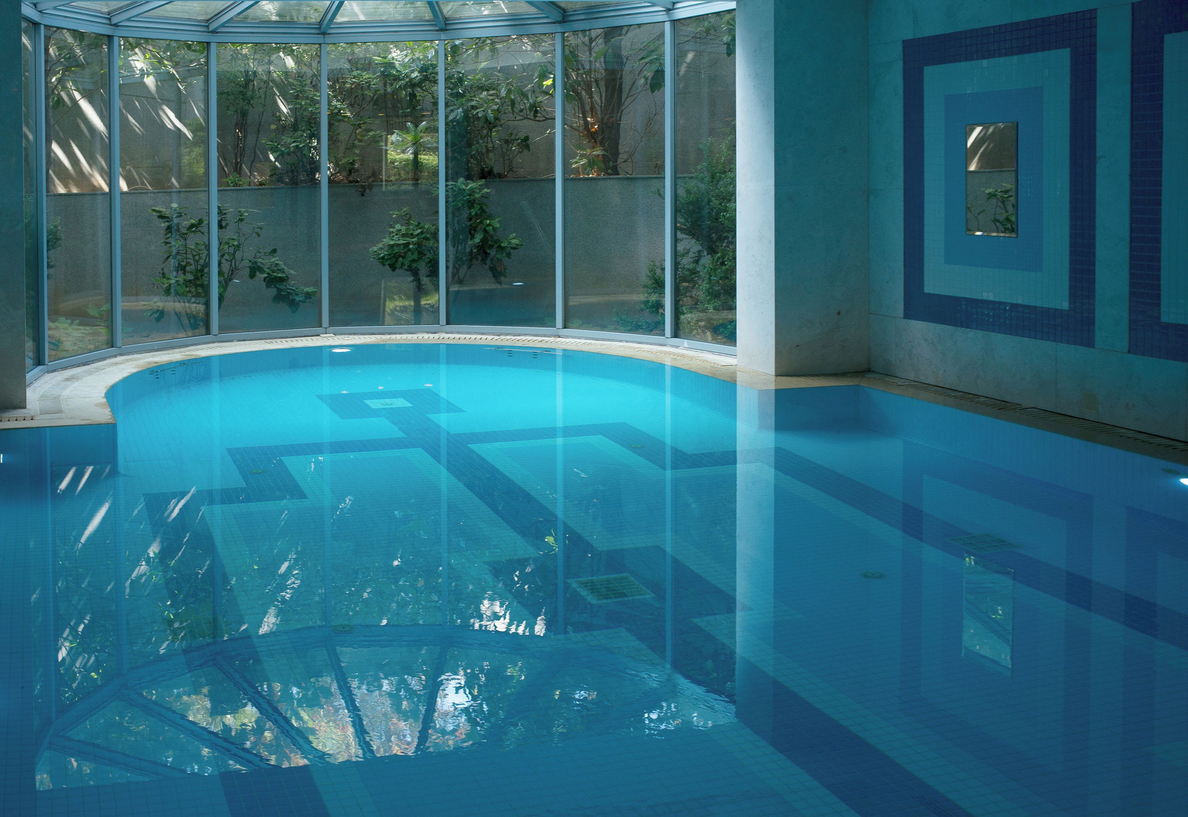 A clear indoor swimming pool with a glass enclosure, surrounded by walls with a geometric pattern.