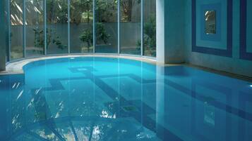 A clear indoor swimming pool with a glass enclosure, surrounded by walls with a geometric pattern.
