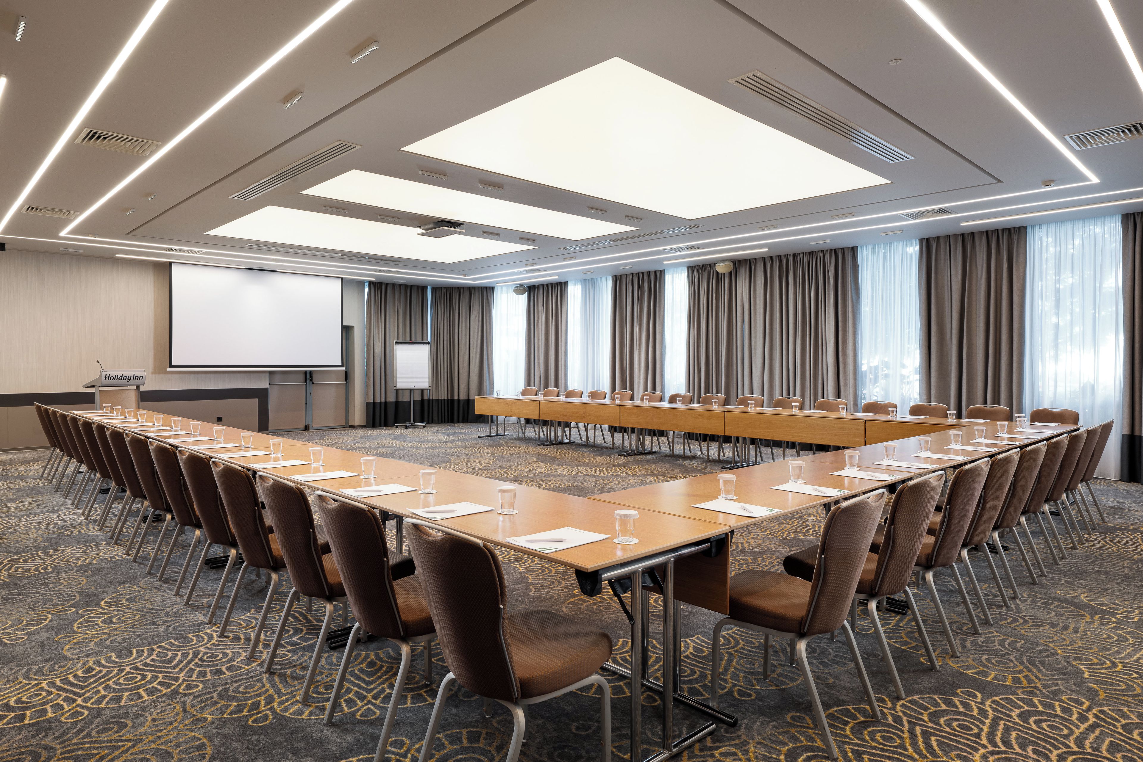 A conference room with a long table, chairs, a projector screen, and a carpeted floor.