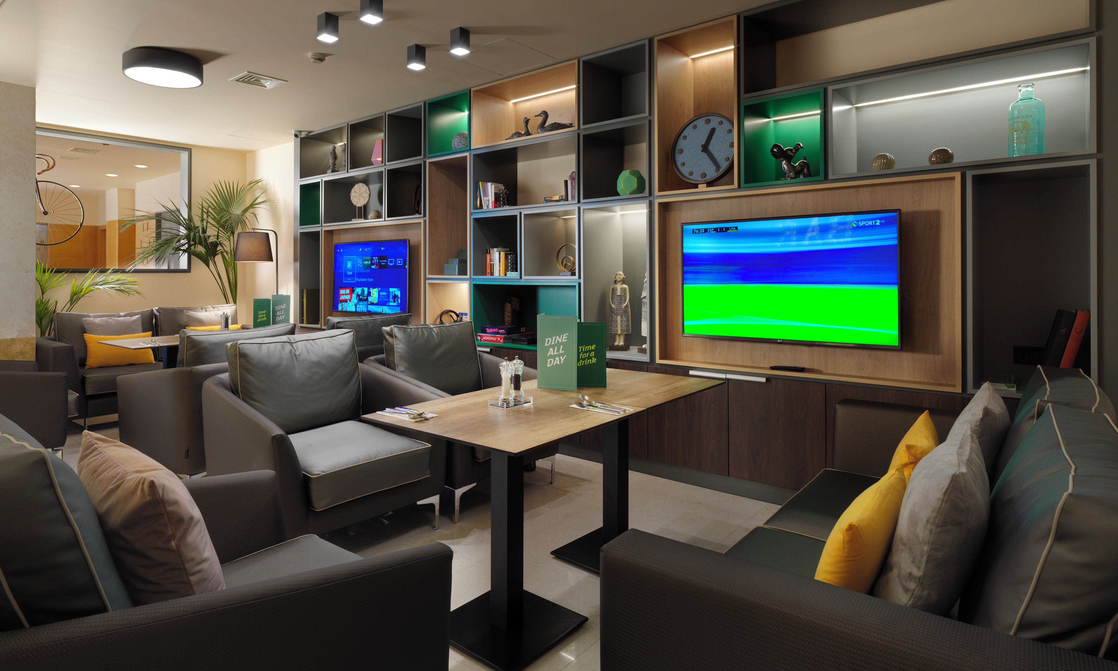 A modern lounge area with seating, a flat-screen TV, and shelves with various items.