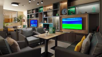 A modern lounge area with seating, a flat-screen TV, and shelves with various items.