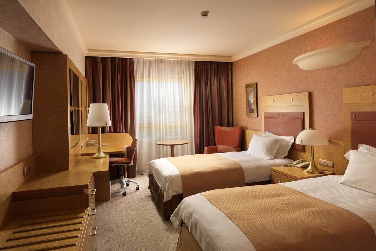 Een hotelkamer met twee bedden, een bureau met stoel, een kleine tafel en een televisie.