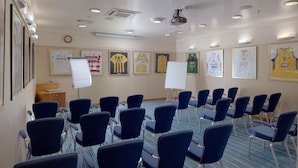 Une salle de conférence avec des rangées de chaises bleues, un tableau blanc et des maillots de sport encadrés accrochés aux murs.