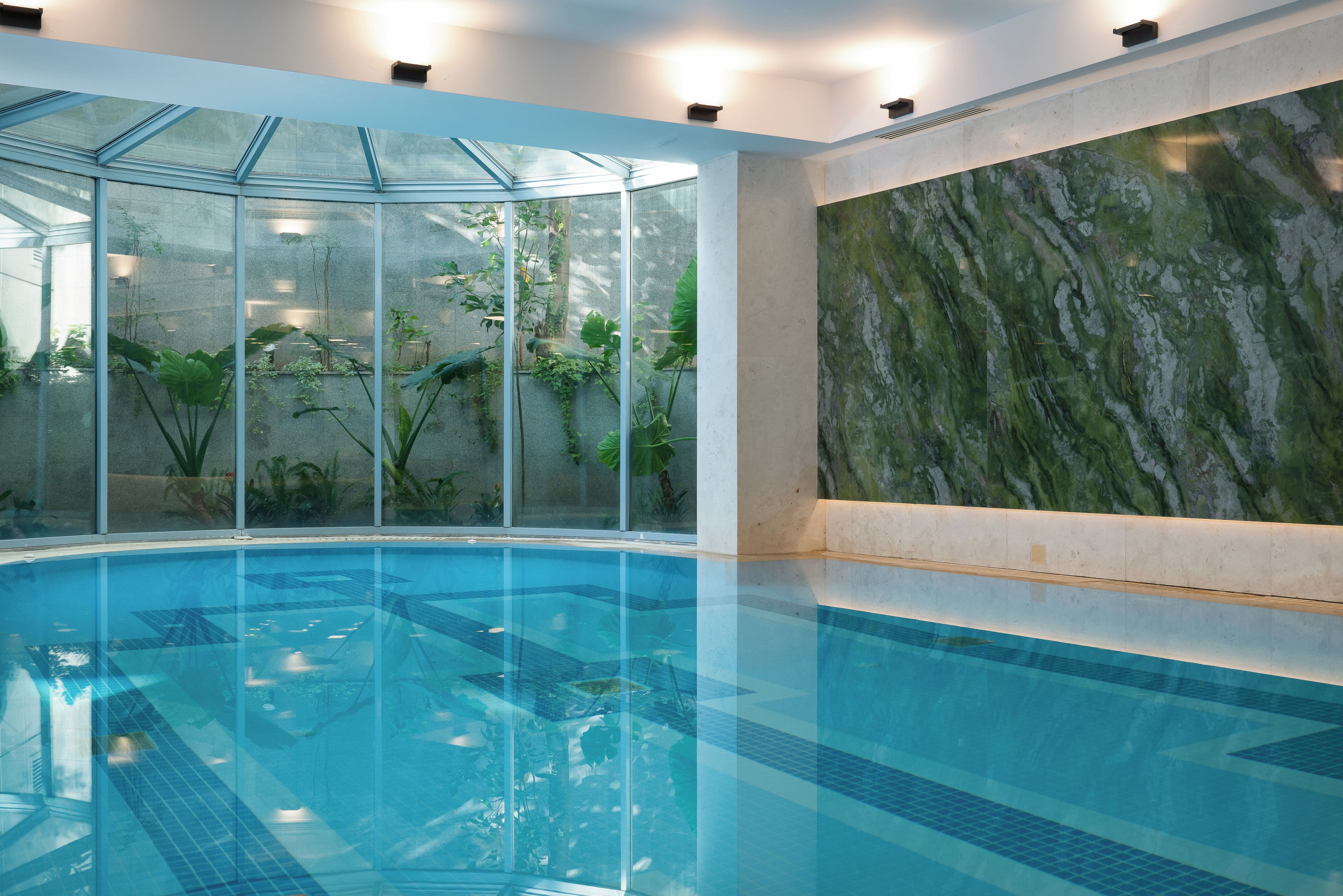 A clear indoor swimming pool with glass walls and a marble wall.