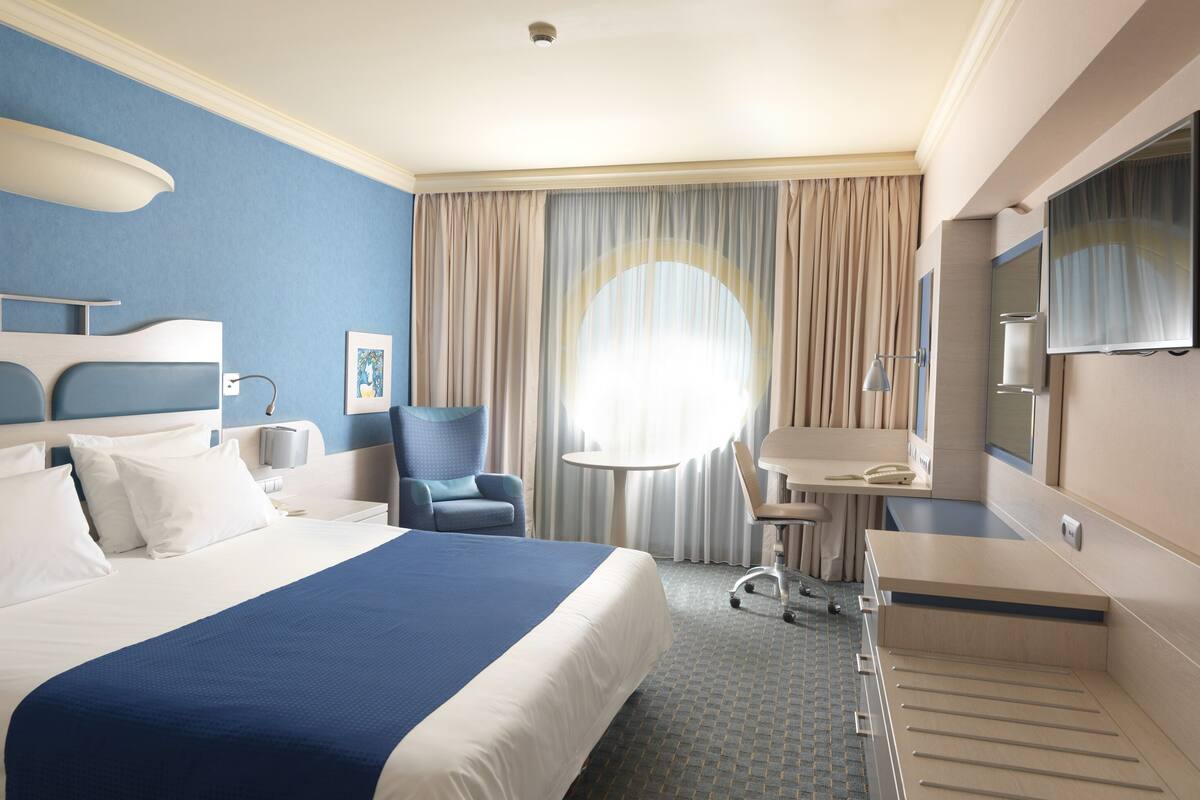 Een hotelkamer met een groot bed, een bureau, een stoel, een televisie en een raam met gordijnen.