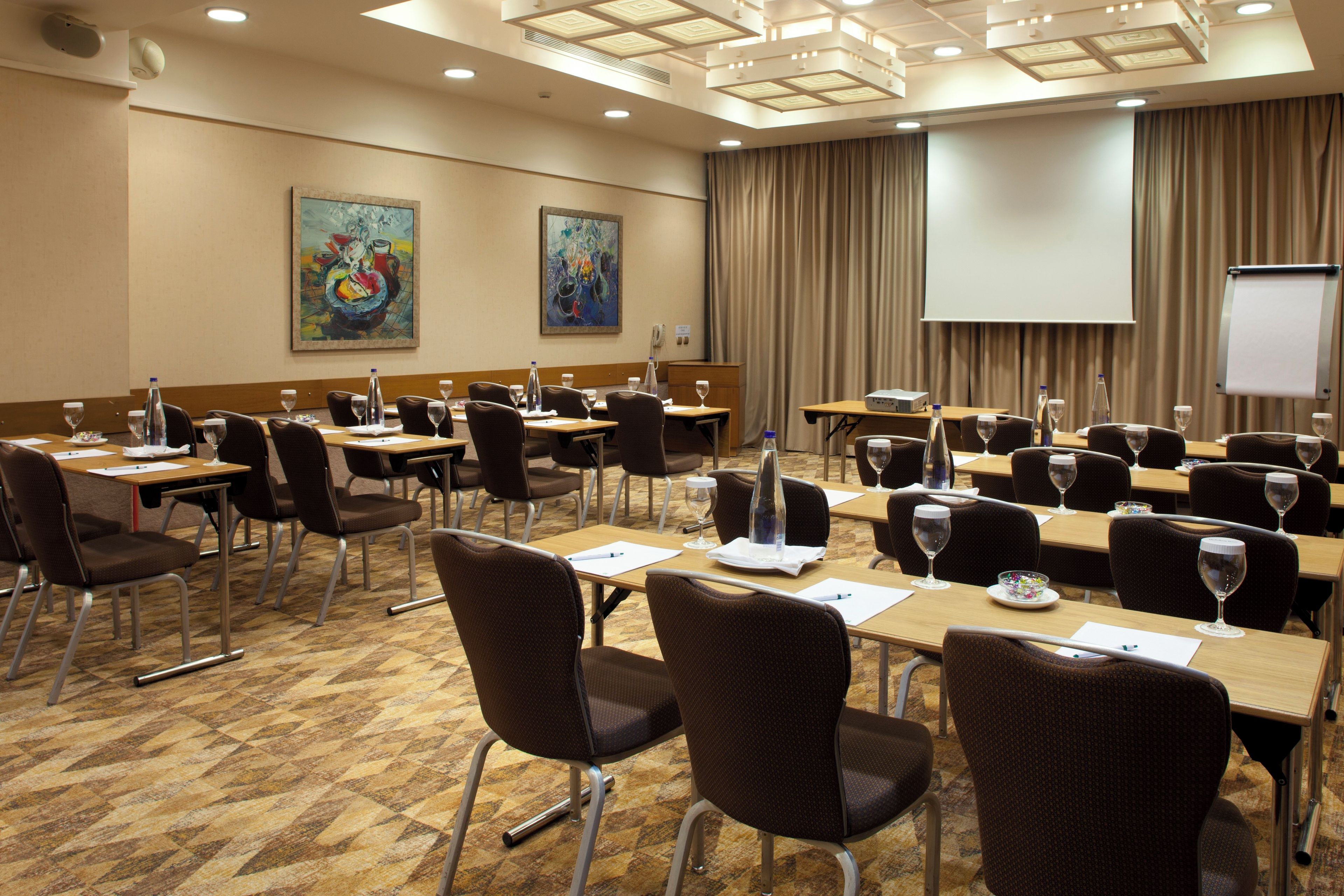 A conference room with multiple tables, chairs, and a projector screen.