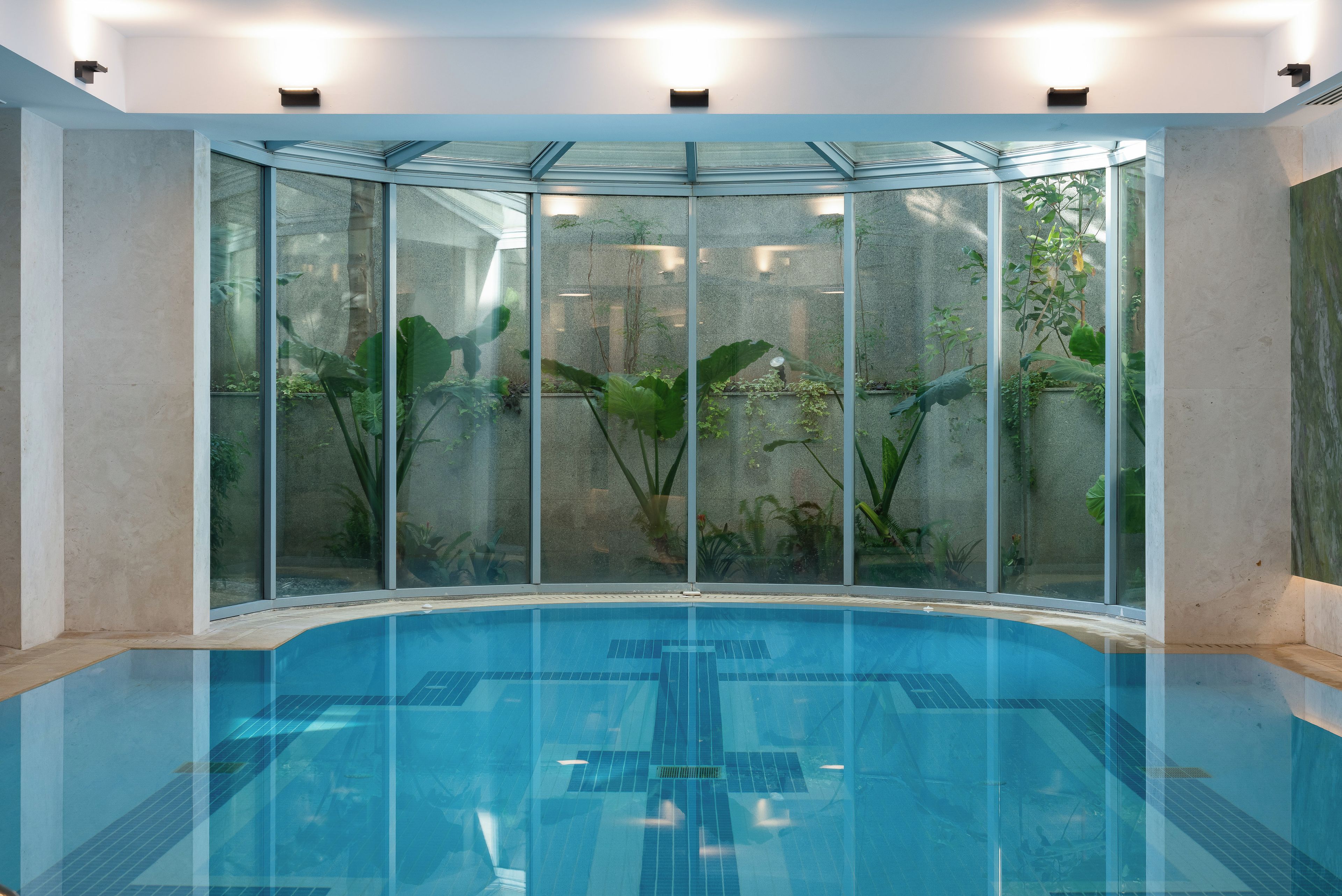 Una piscina interna in vetro con acqua cristallina, circondata da pareti con piante e vista sull'esterno.