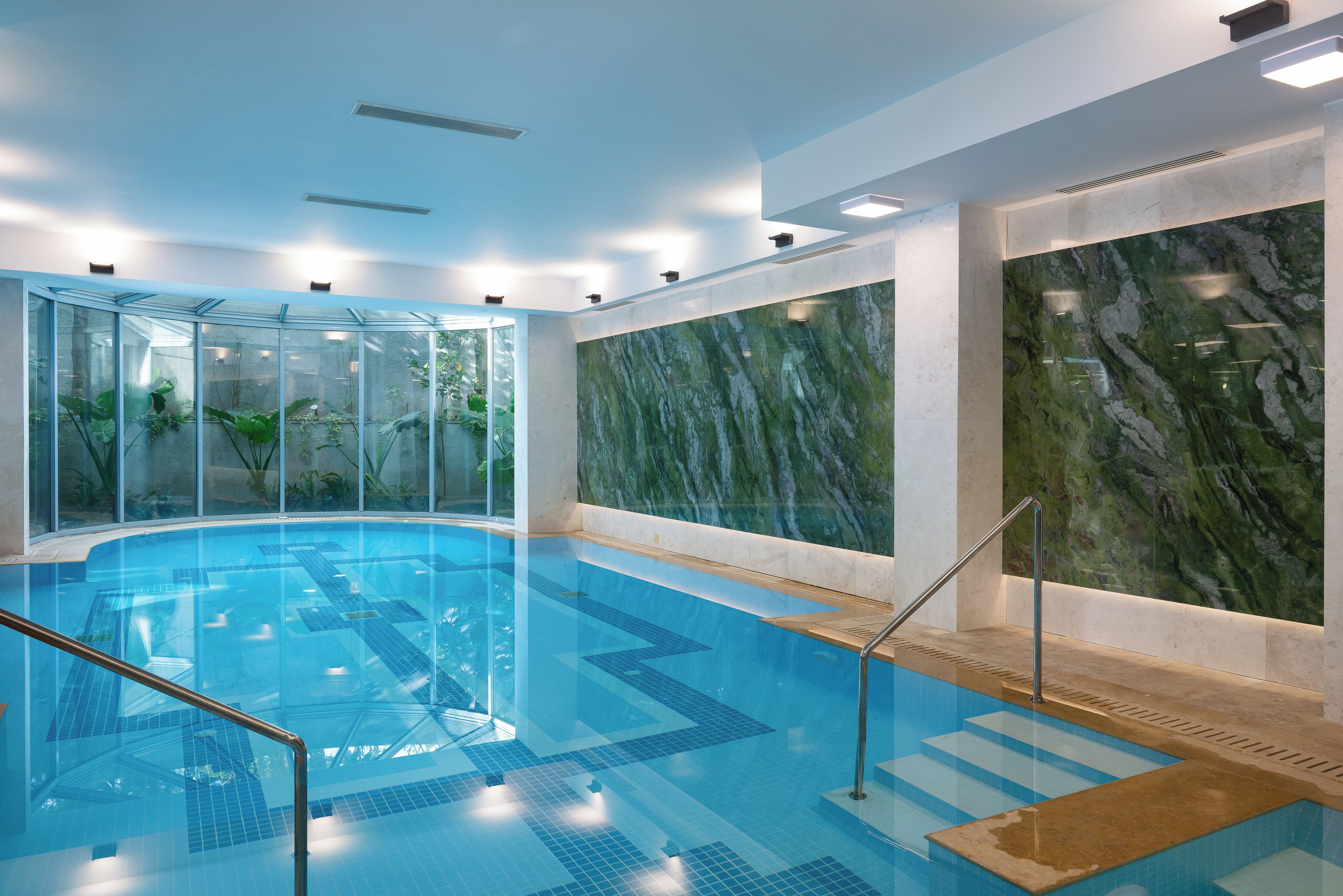 An indoor swimming pool with clear glass walls, a marble wall, and a tiled floor.