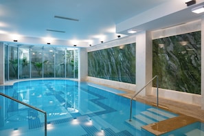 Una piscina interior con paredes de vidrio transparente, pared de mármol y suelo de baldosas.