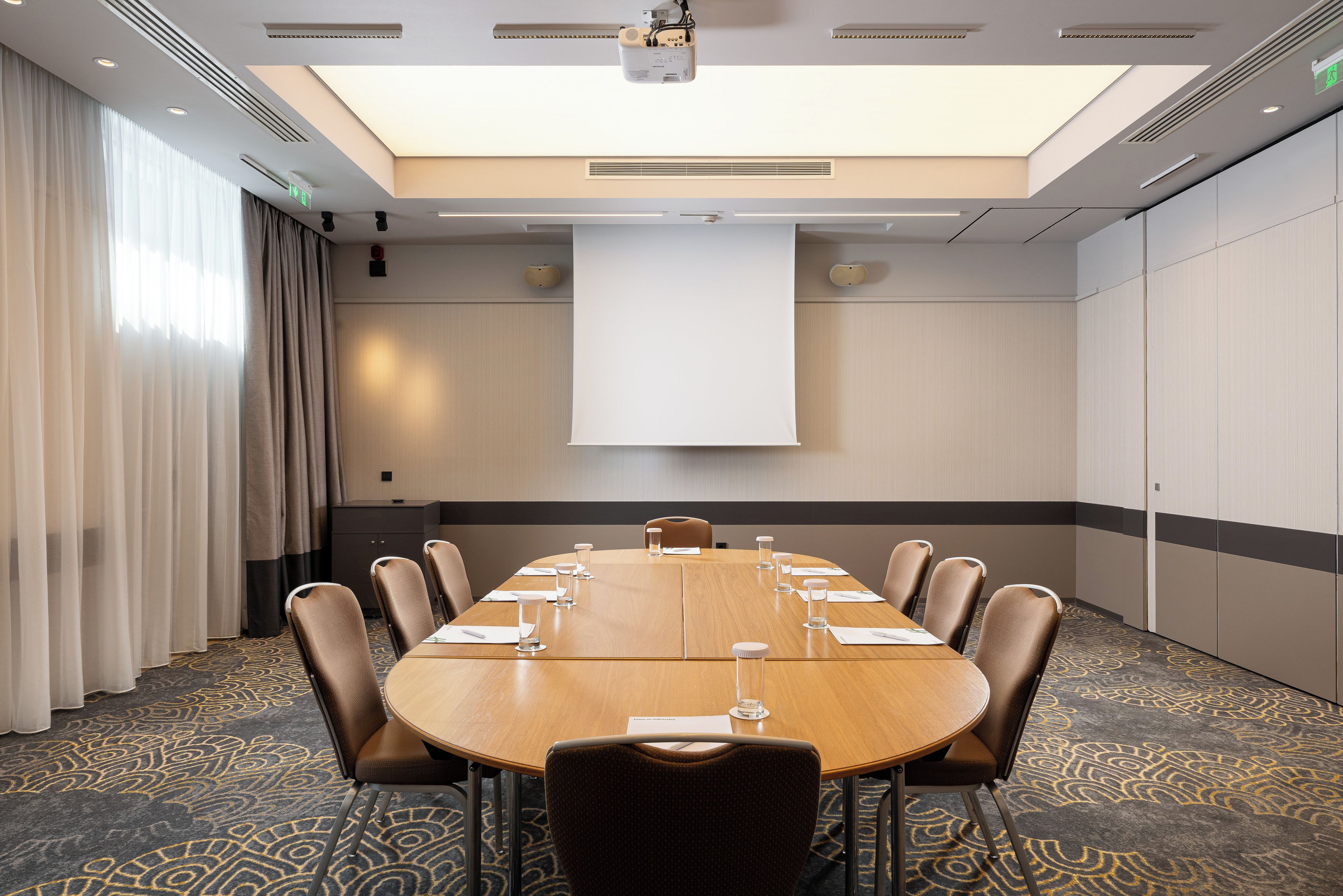 Une salle de conférence équipée d’une grande table, de chaises, d’un écran de projection et d’un tapis à motifs.
