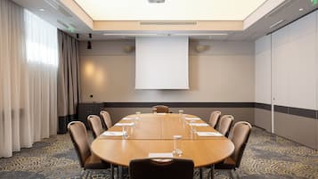 Une salle de conférence équipée d’une grande table, de chaises, d’un écran de projection et d’un tapis à motifs.