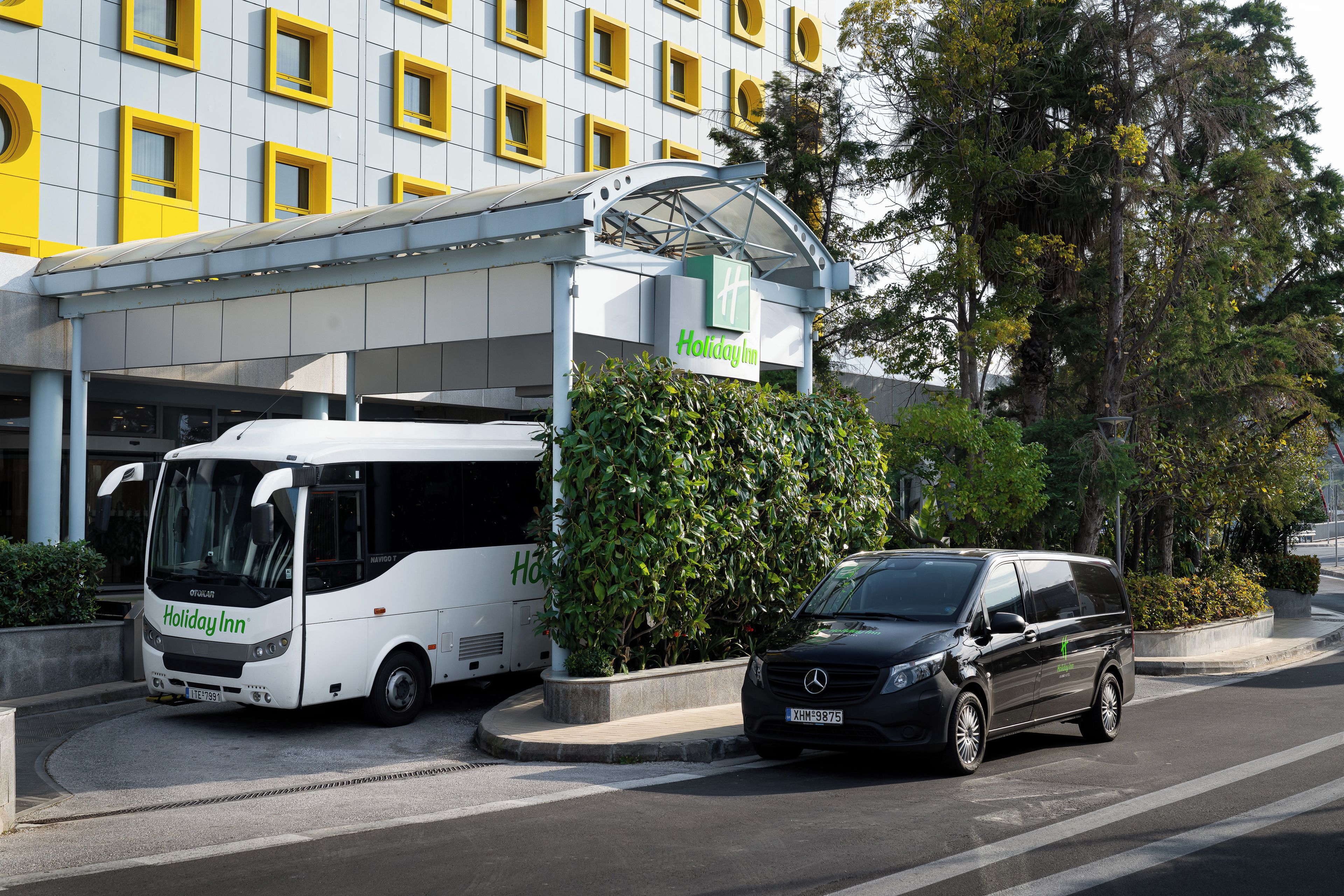 A Holiday Inn hotel with a bus and a black car parked in front.