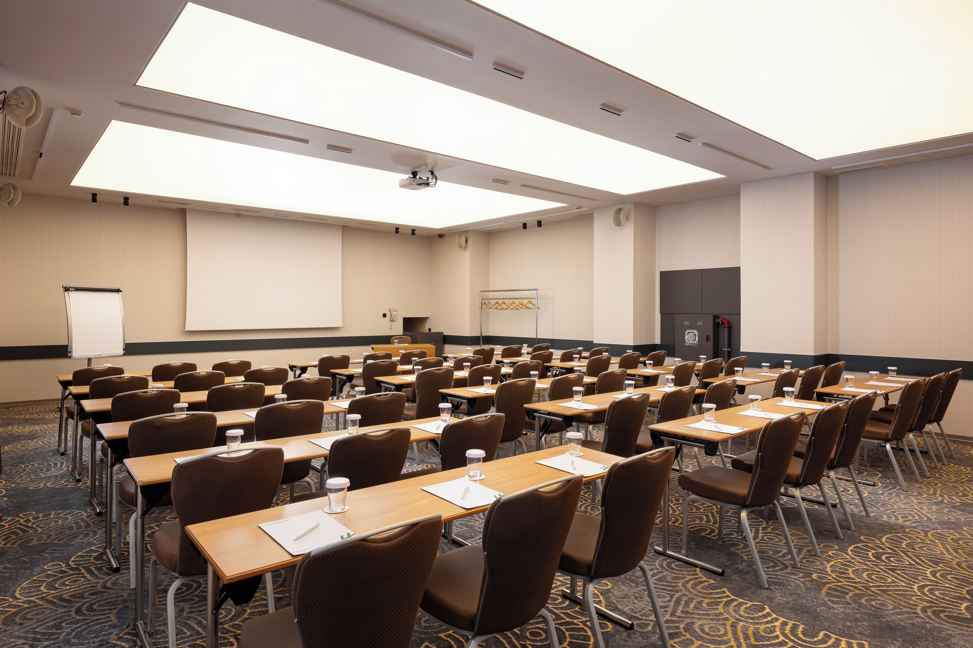 A conference room with rows of tables and chairs, a projector screen, and a whiteboard.