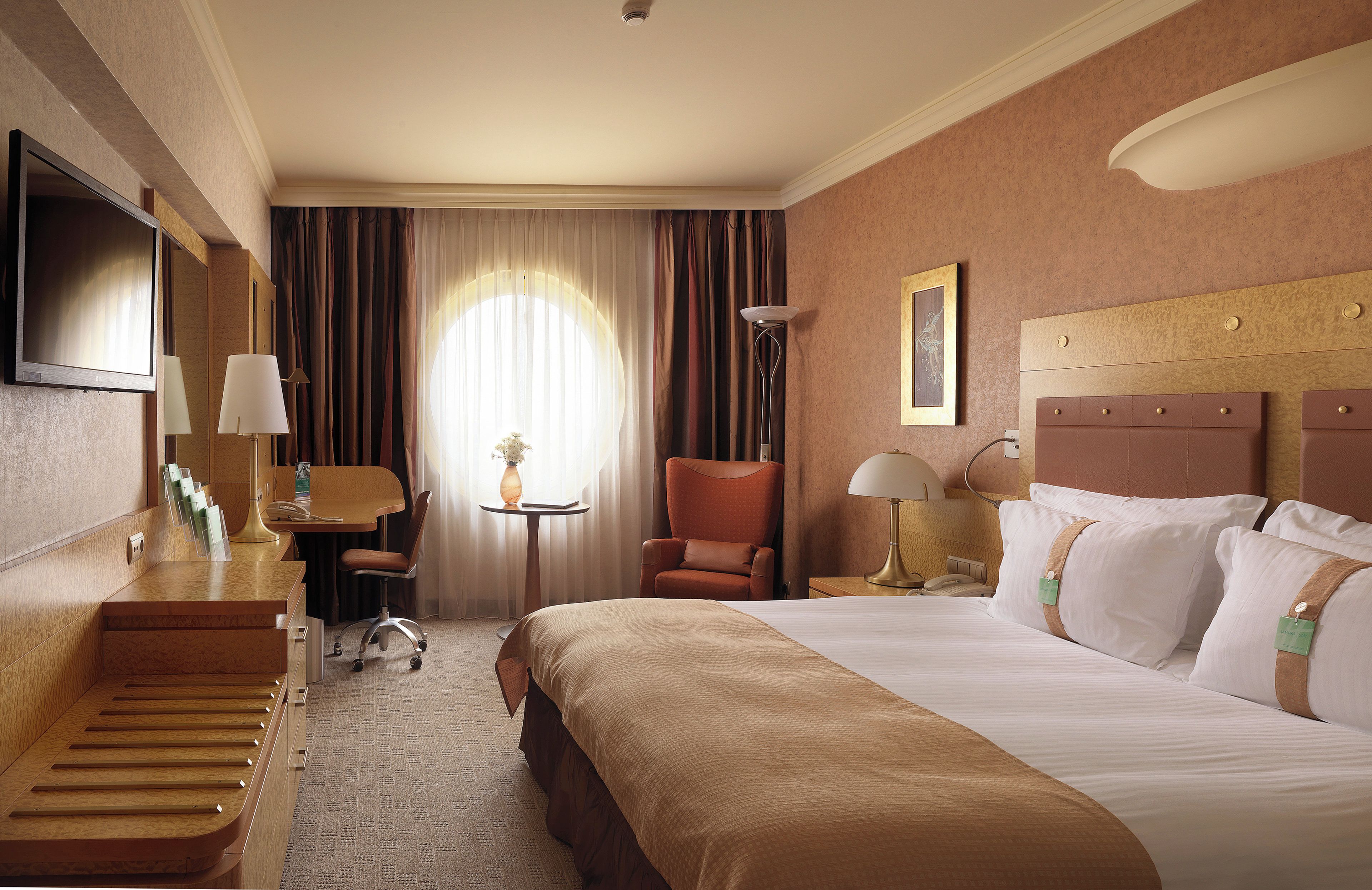 A hotel room with a bed, a desk, a chair, a television, and a window with curtains.