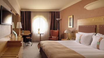 Quarto de hotel com cama, escrivaninha, cadeira, televisão e janela com cortinas.