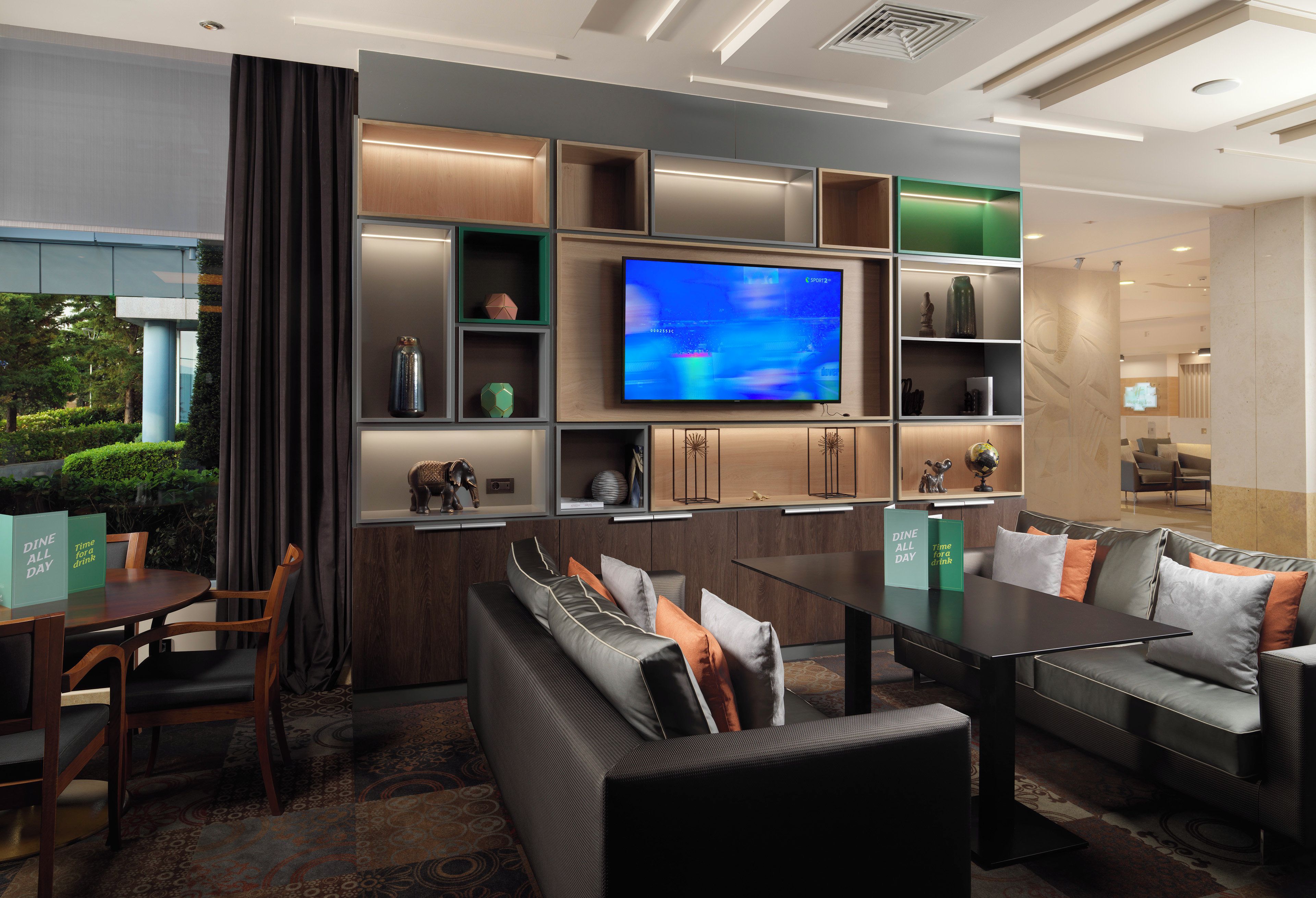 Eine moderne Hotelhalle mit Sitzgelegenheiten, einem Flachbildfernseher und einer Rezeption.
