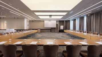 Un salón de conferencias con una larga mesa, sillas, una pantalla de proyector y piso alfombrado.