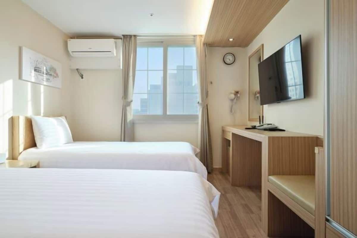 Quarto de hotel com duas camas, uma escrivaninha, televisão e janela com cortinas.