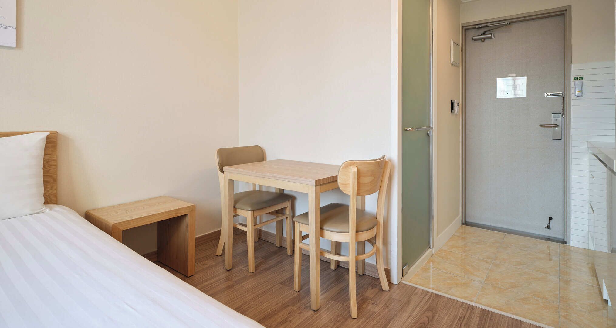 Un dormitorio con cama, una mesita de noche, un escritorio de madera con dos sillas y una zona de ducha.