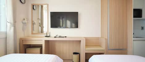 Une chambre d’hôtel équipée d’un bureau, de deux lits, d’un miroir, d’une horloge, d’une télévision et d’une kitchenette.