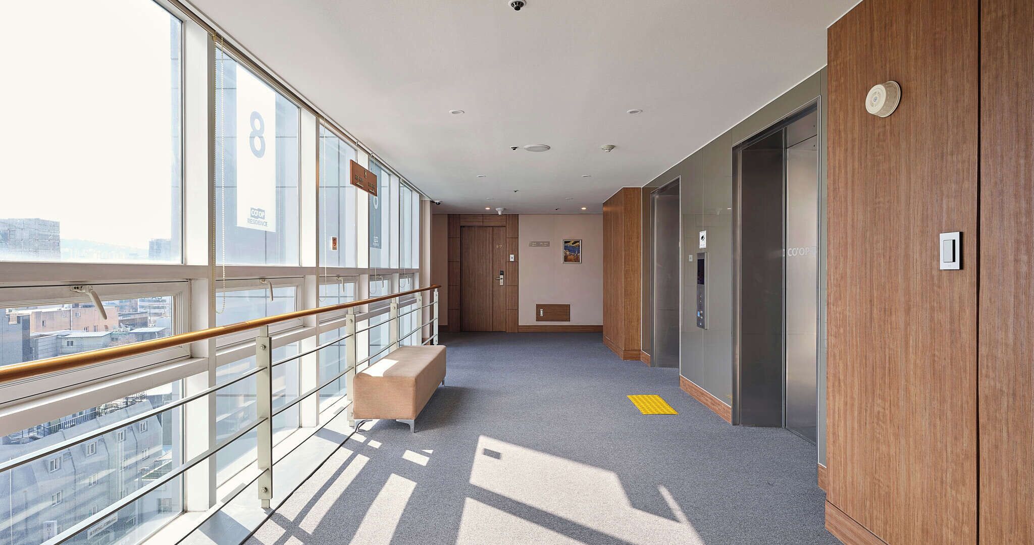 A corridor with a bench, glass walls, and a view of buildings.