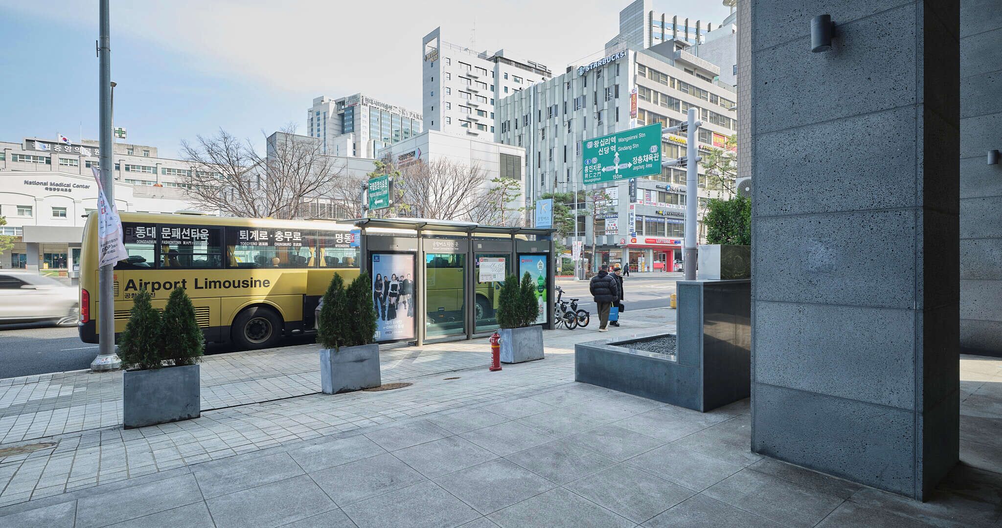 A bus stop with a shelter, a taxi, and a building with signage in a city environment.