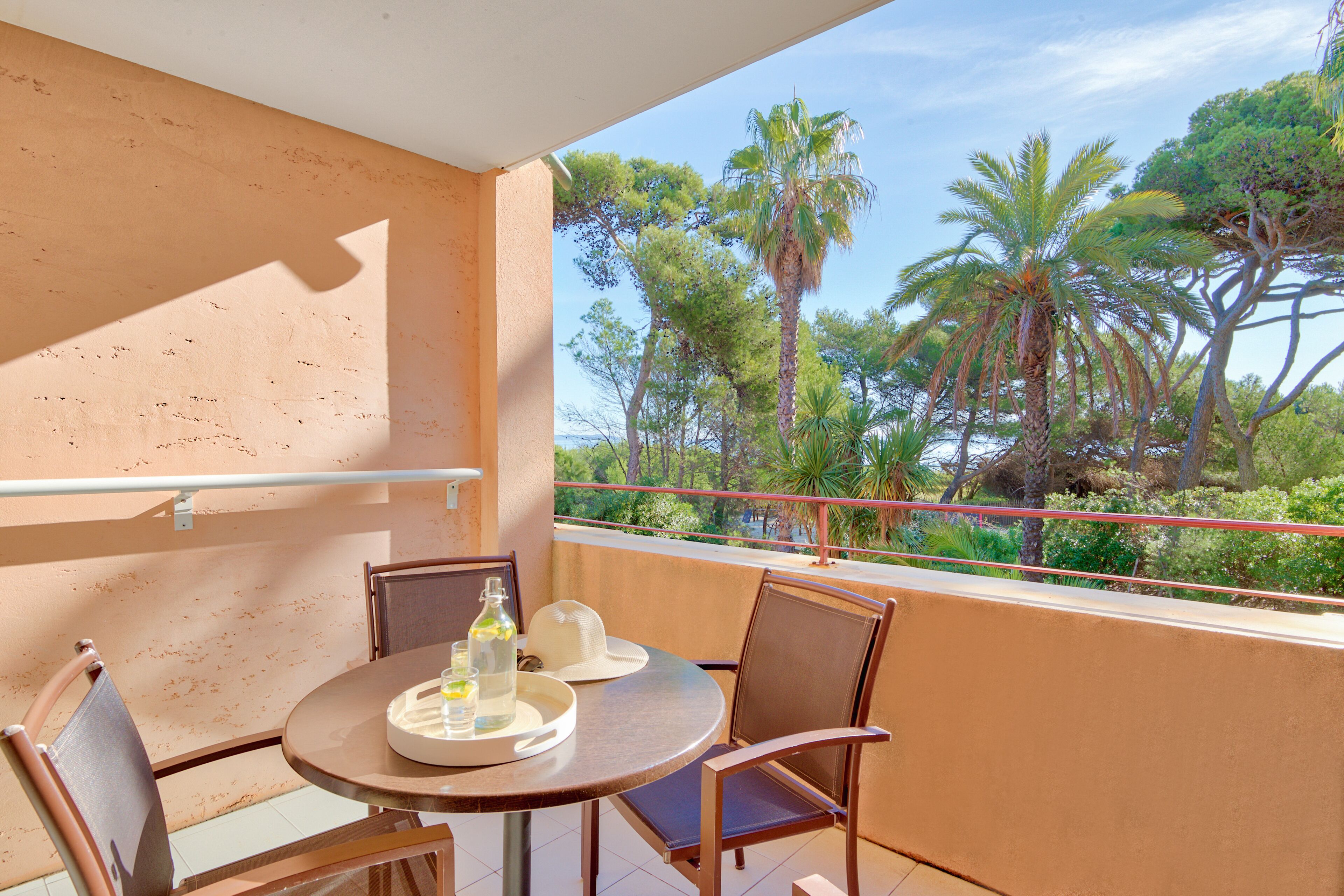 A balcony with a table and chairs, overlooking a garden with palm trees.