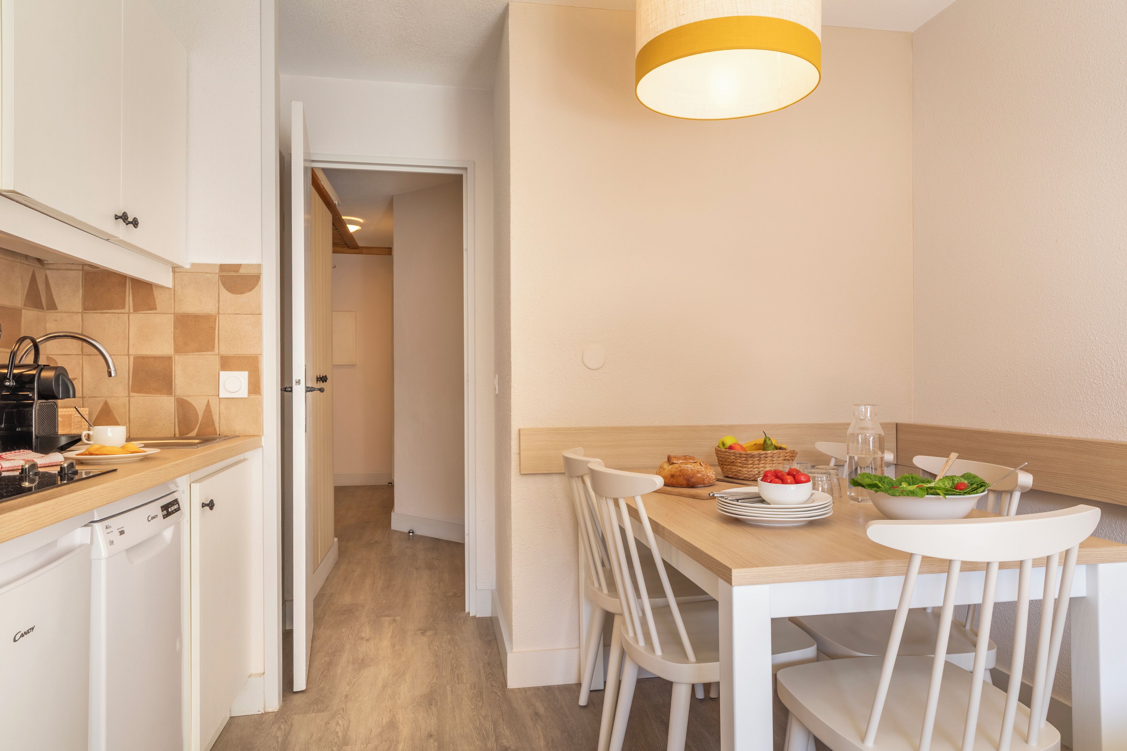 A modern kitchen with white cabinets, a wooden countertop, and a dining area with a table set for two.