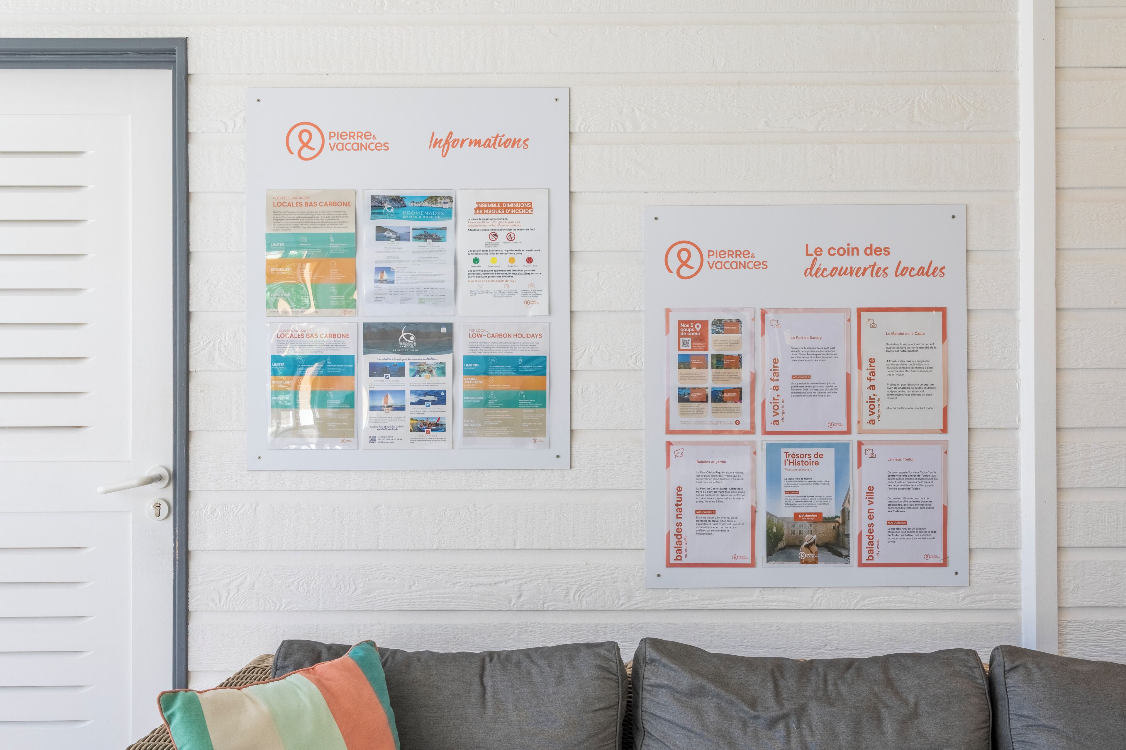 A bulletin board with information on local attractions and events, a white door, and a grey couch.