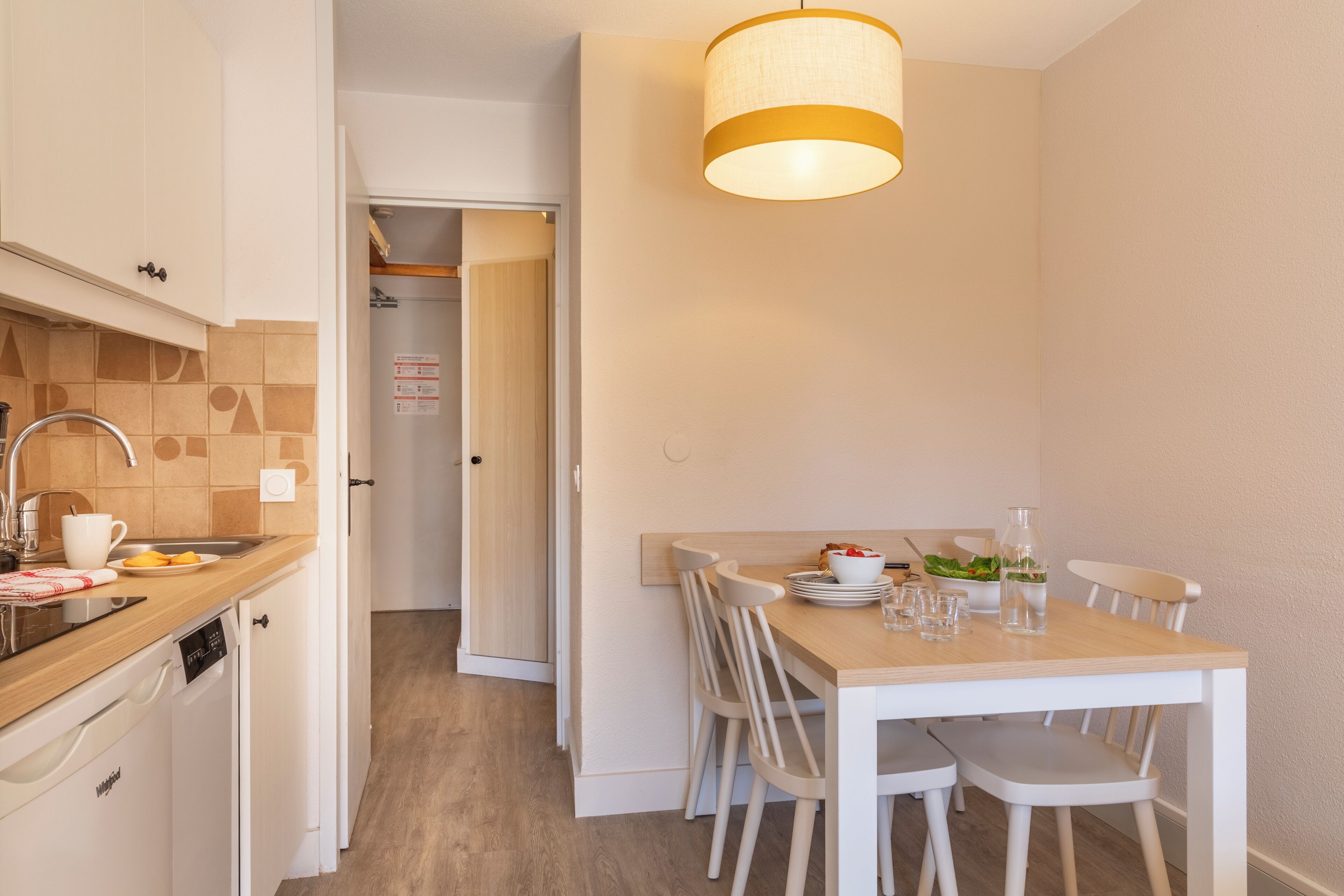 Una cucina compatta con mobili bianchi, un piano di lavoro in legno e un'area pranzo con tavolo e sedie.