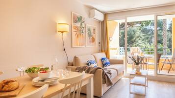 Ein modernes Wohnzimmer mit Essbereich, einer Couch, einem Couchtisch und einem Balkon mit Gartenmöbeln.