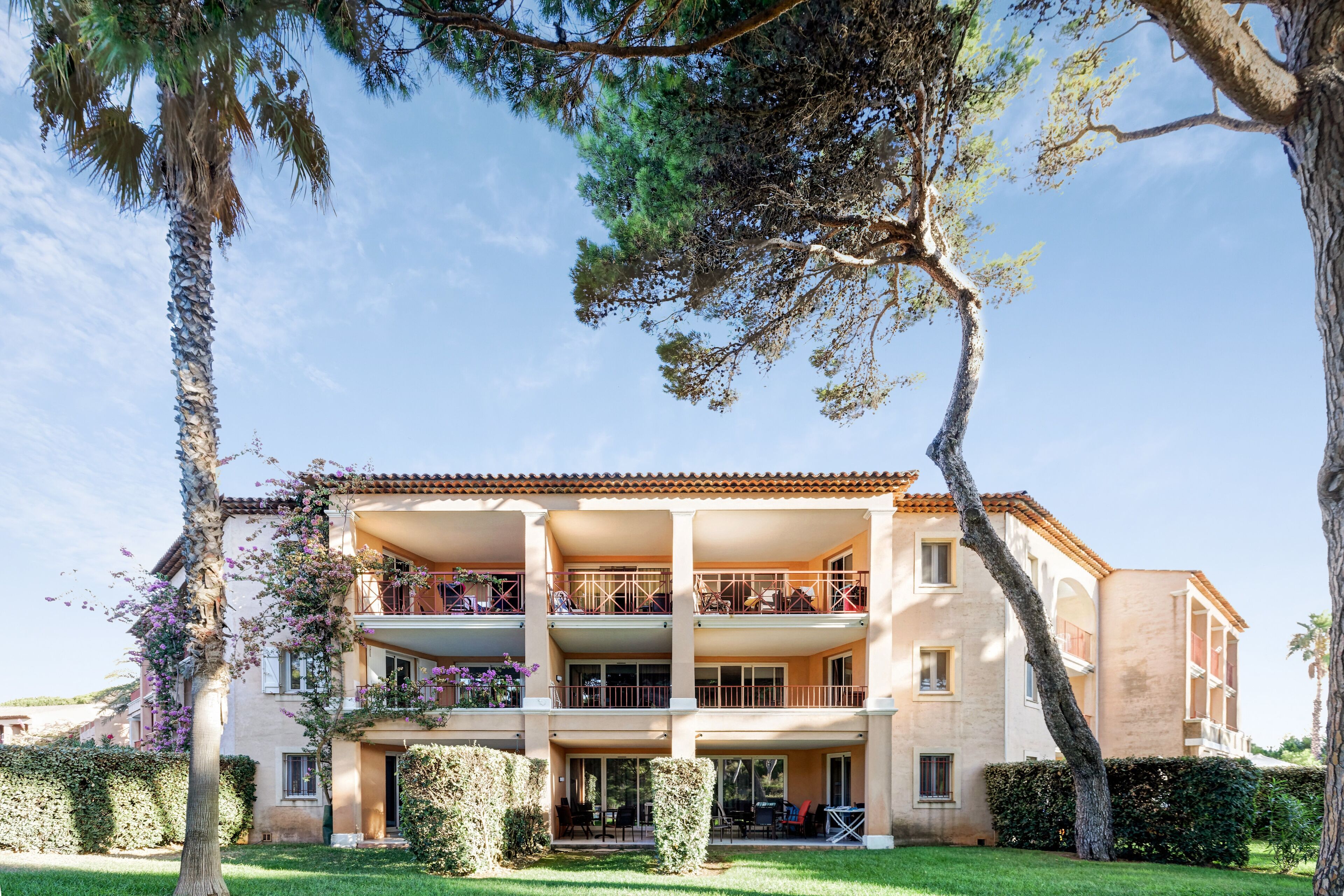 A multi-story building with balconies, a garden, and a clear sky.