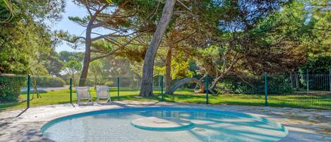 Une piscine dotée d’une plage en pierre, entourée d’une clôture et d’arbres.
