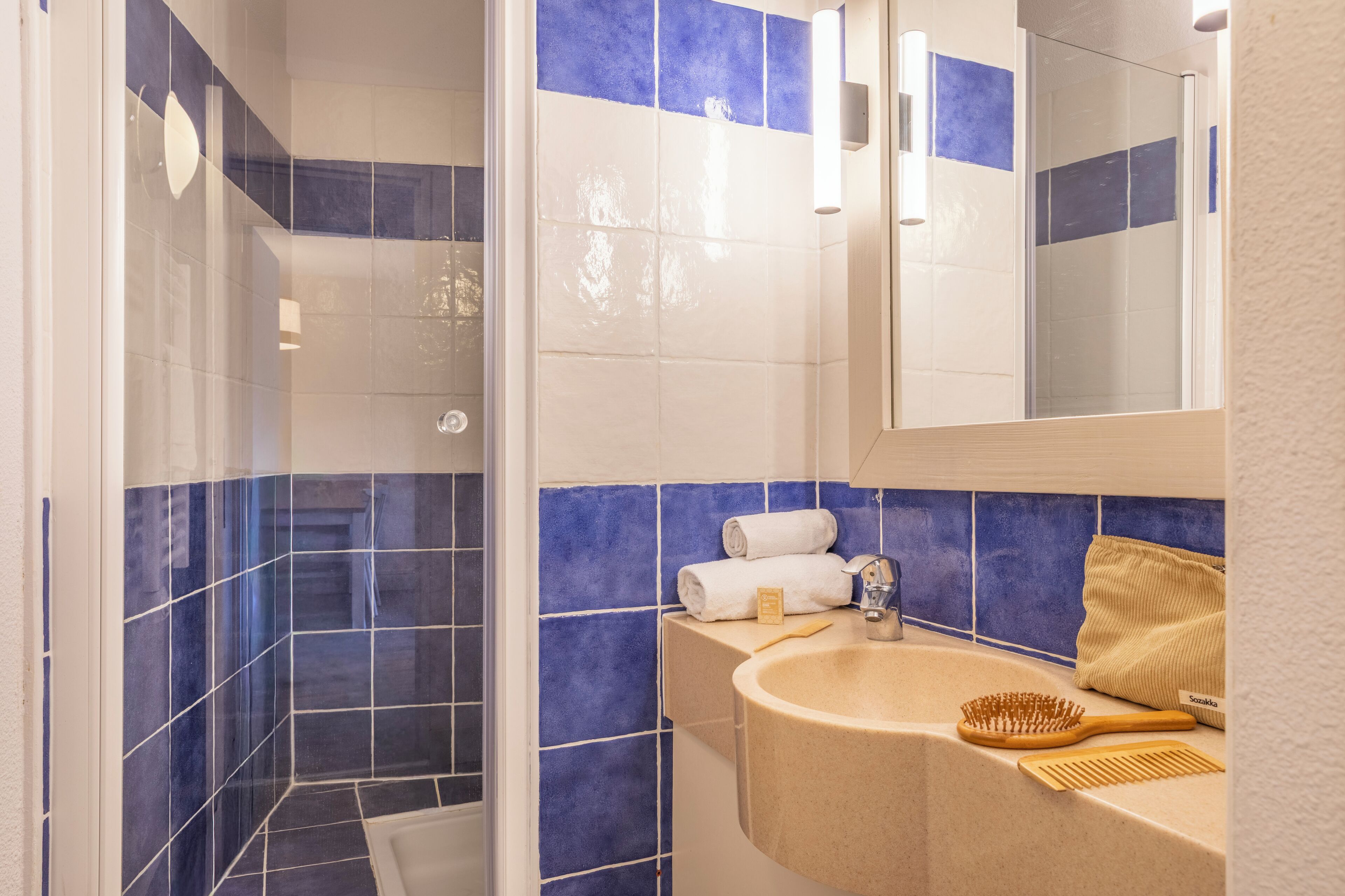 Un bagno con piastrelle blu e bianche, un lavandino, uno specchio e una doccia.
