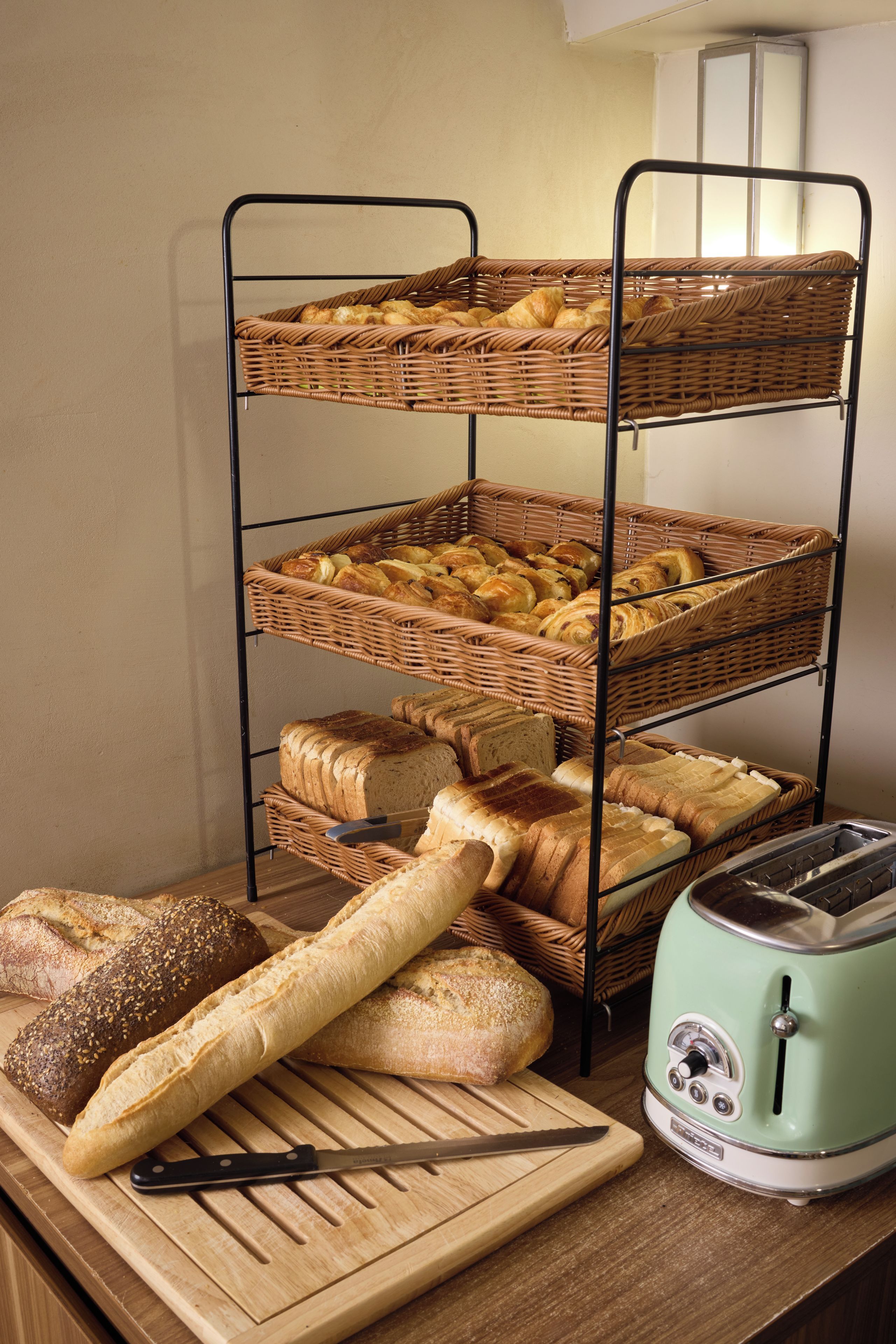 Ein mehrstufiges Brotregal mit verschiedenen Brotsorten und einem Toaster auf einer Holztischplatte.