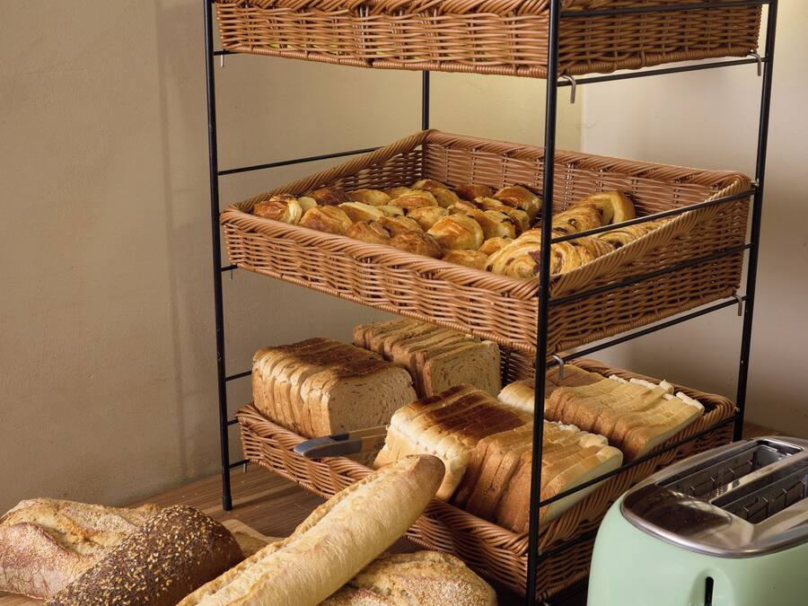 Un présentoir à pain à plusieurs niveaux, avec différents types de pain et un grille-pain, le tout posé sur une surface en bois.