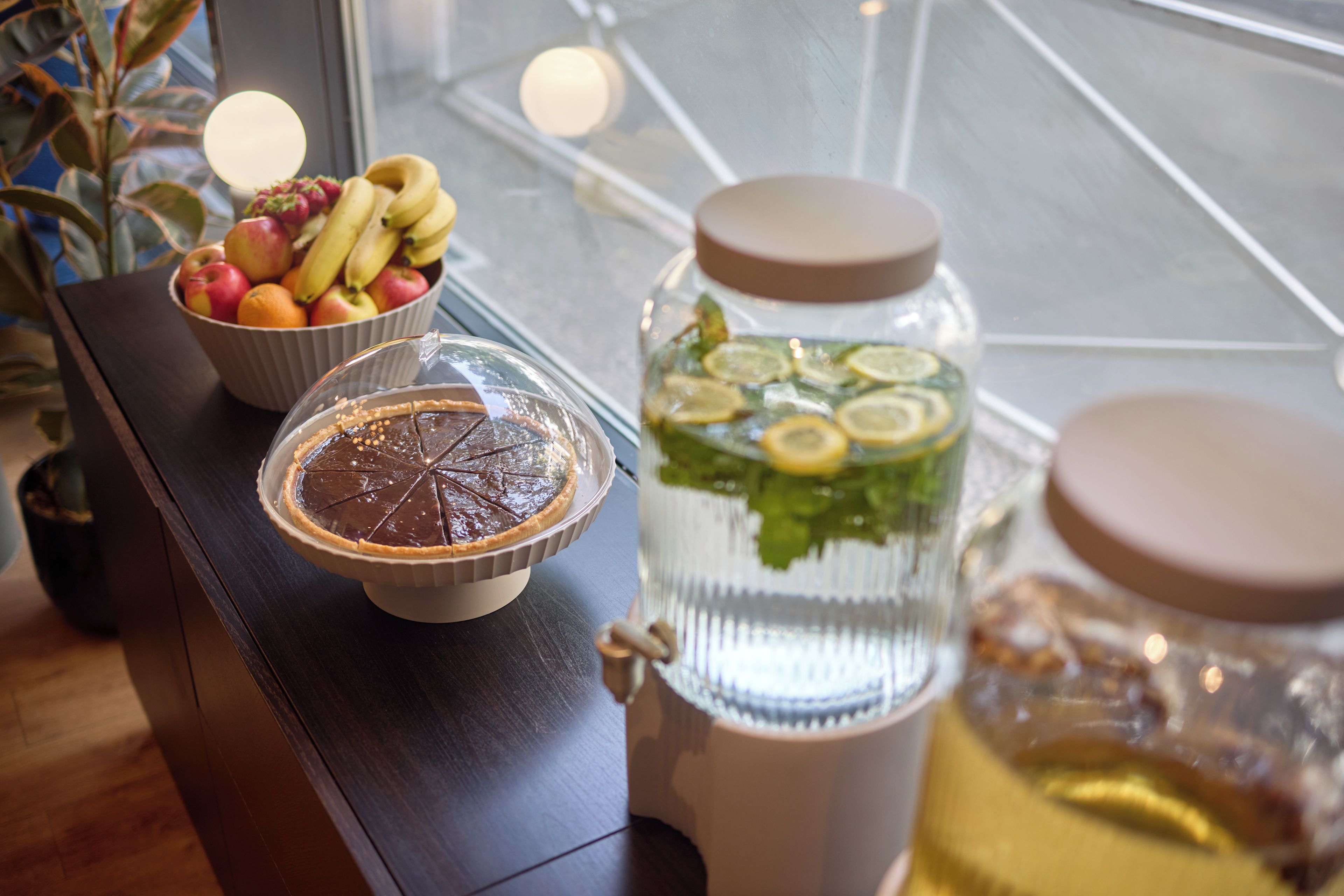 A table with a pie, a bowl of fruit, and a water dispenser.