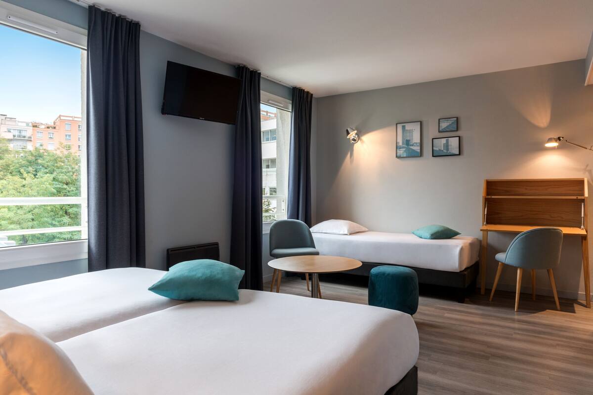 Une chambre d’hôtel avec deux lits, un bureau, une chaise et une petite table.