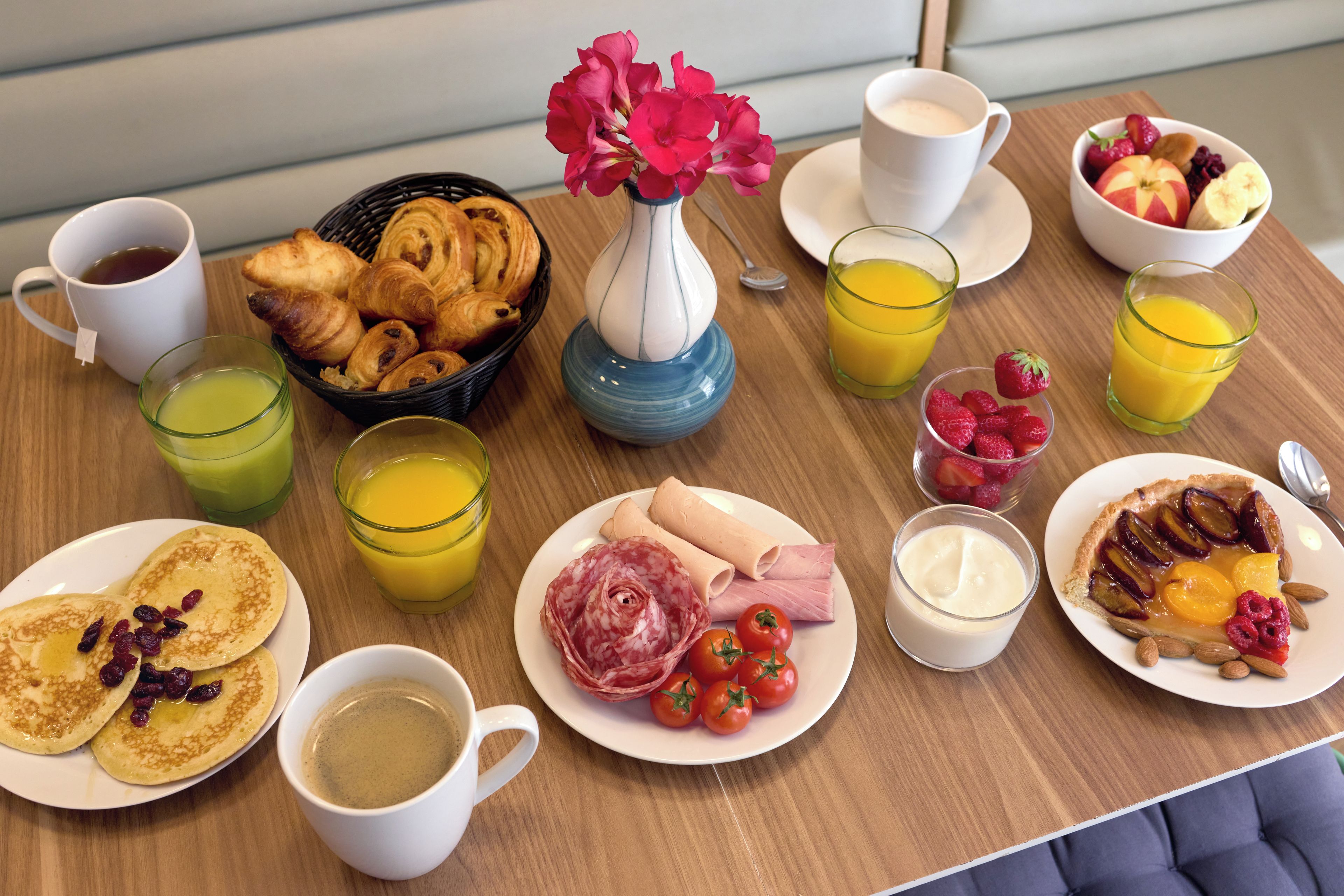 A breakfast table with croissants, pastries, fruit, juice, and coffee.