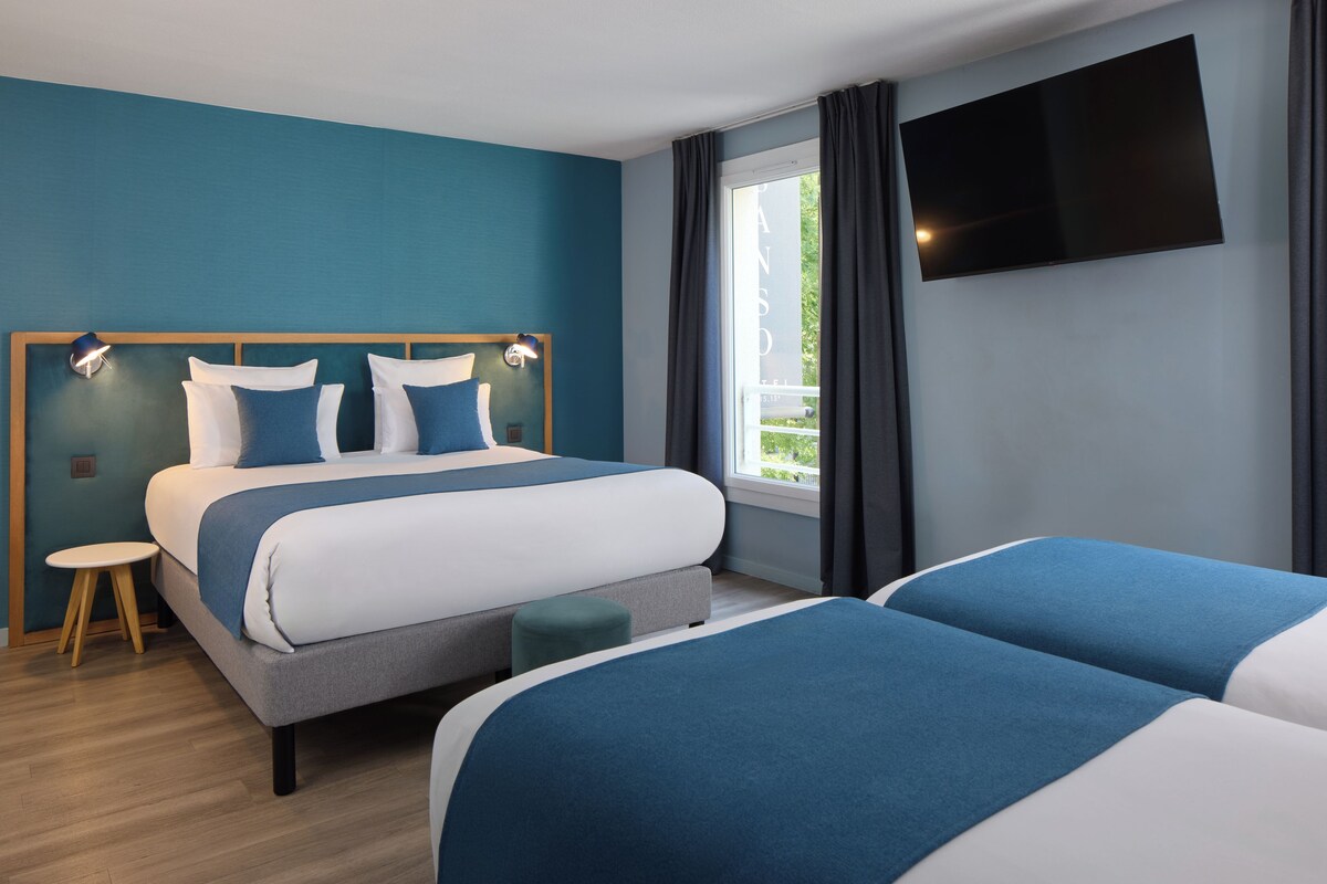 A hotel room with a bed, bedside tables, a TV, and a window with curtains.