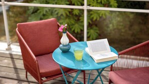 A red chair, a blue table with a book and a glass of yellow liquid, and a white vase with pink flowers on a balcony. - Hôtel Sanso by HappyCulture (Ex Quality Bercy Bibliotèque) (Paris)