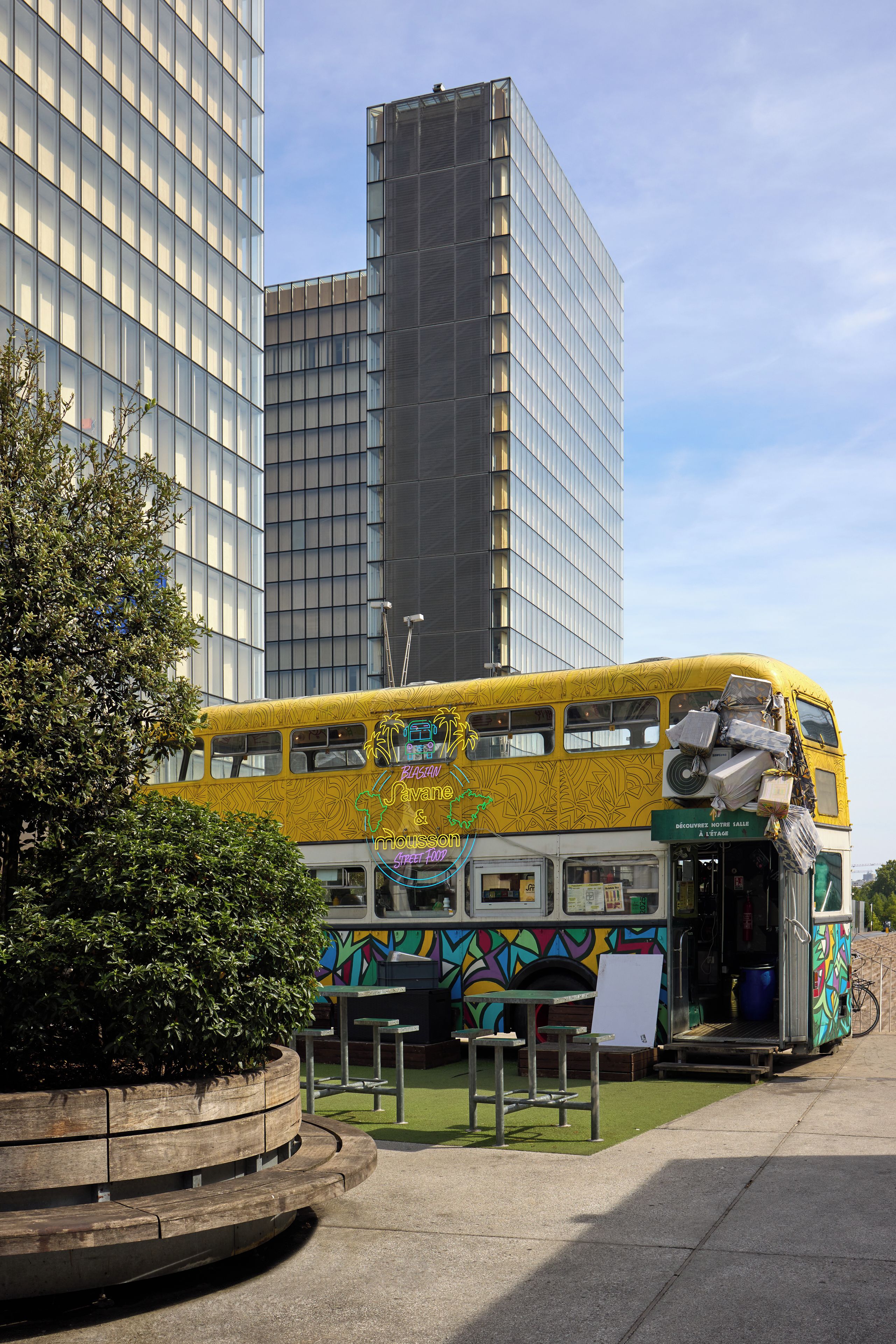 A double-decker bus with a colorful mural, parked in front of a modern building.