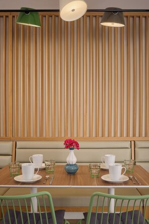 A dining area with a wooden slat wall, a table set with white cups and saucers, a vase with flowers, and green chairs. - Hôtel Sanso by HappyCulture (Ex Quality Bercy Bibliotèque) (Paris)