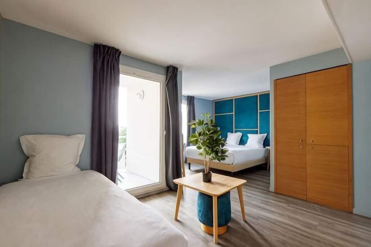 Une chambre d’hôtel comprenant un lit, une table de chevet avec une plante, une armoire et une porte coulissante donnant sur un balcon.