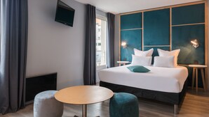 Une chambre d’hôtel moderne avec un grand lit, une petite table ronde et un téléviseur fixé au mur.