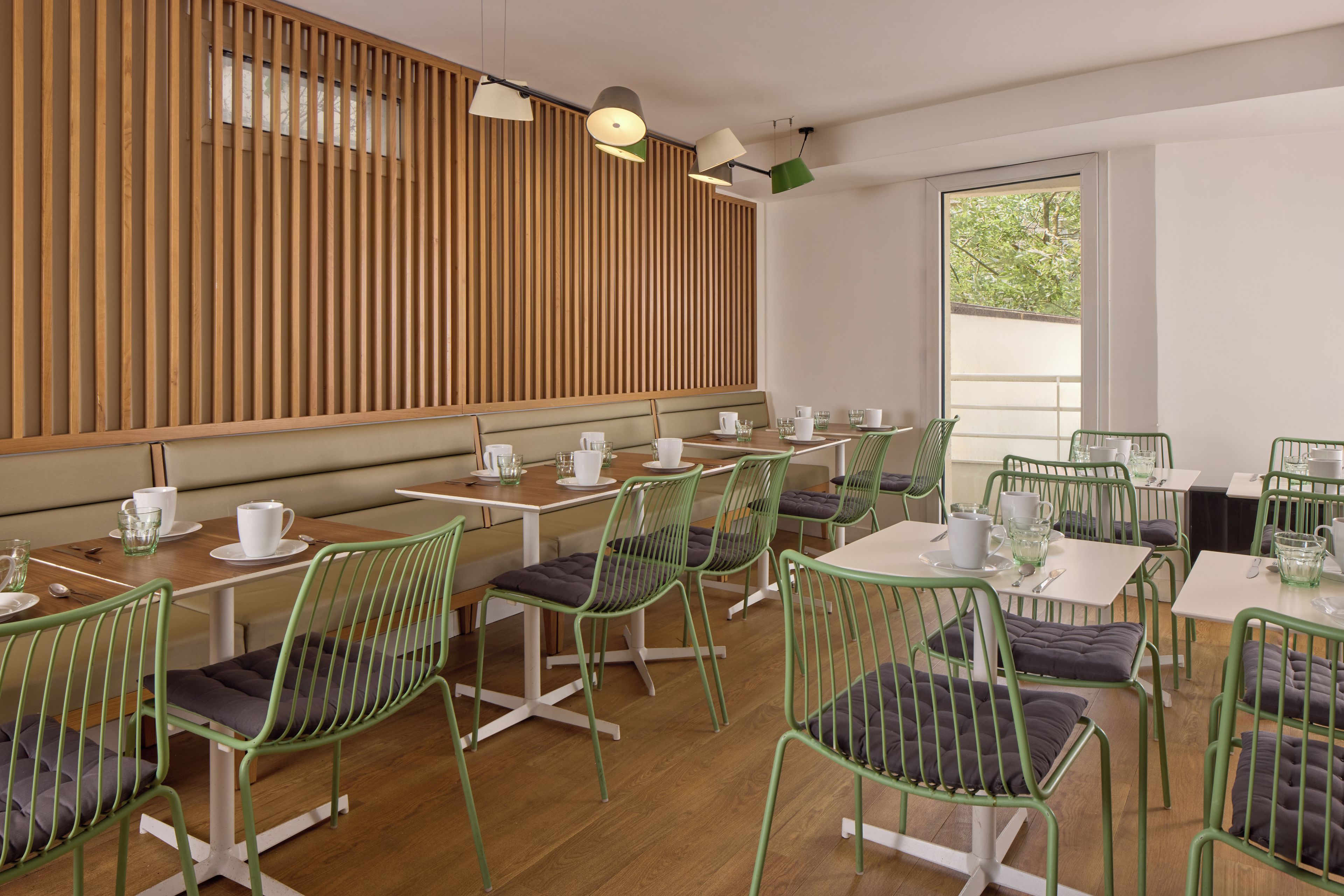 Una cafetería moderna con paredes de listones de madera, sillas de metal verde y mesas blancas.