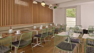 Un café moderne avec des murs aux lambris en bois, des chaises en métal vert et des tables blanches.