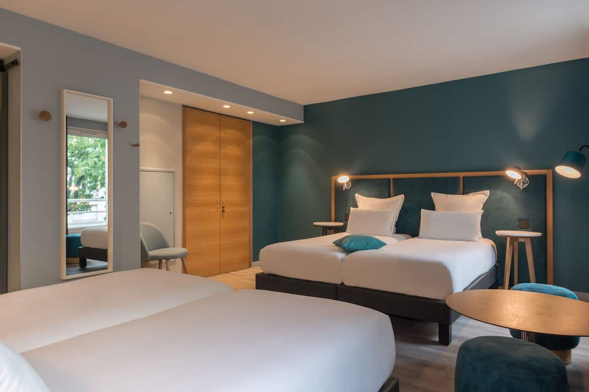 Une chambre d’hôtel moderne avec un grand lit, deux tables de chevet, un miroir et une petite table ronde.