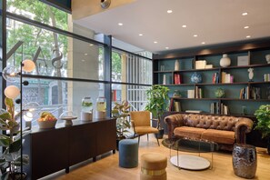 A modern interior with a leather sofa, bookshelves, and a dining area with a fruit bowl. - Hôtel Sanso by HappyCulture (Ex Quality Bercy Bibliotèque) (Paris)