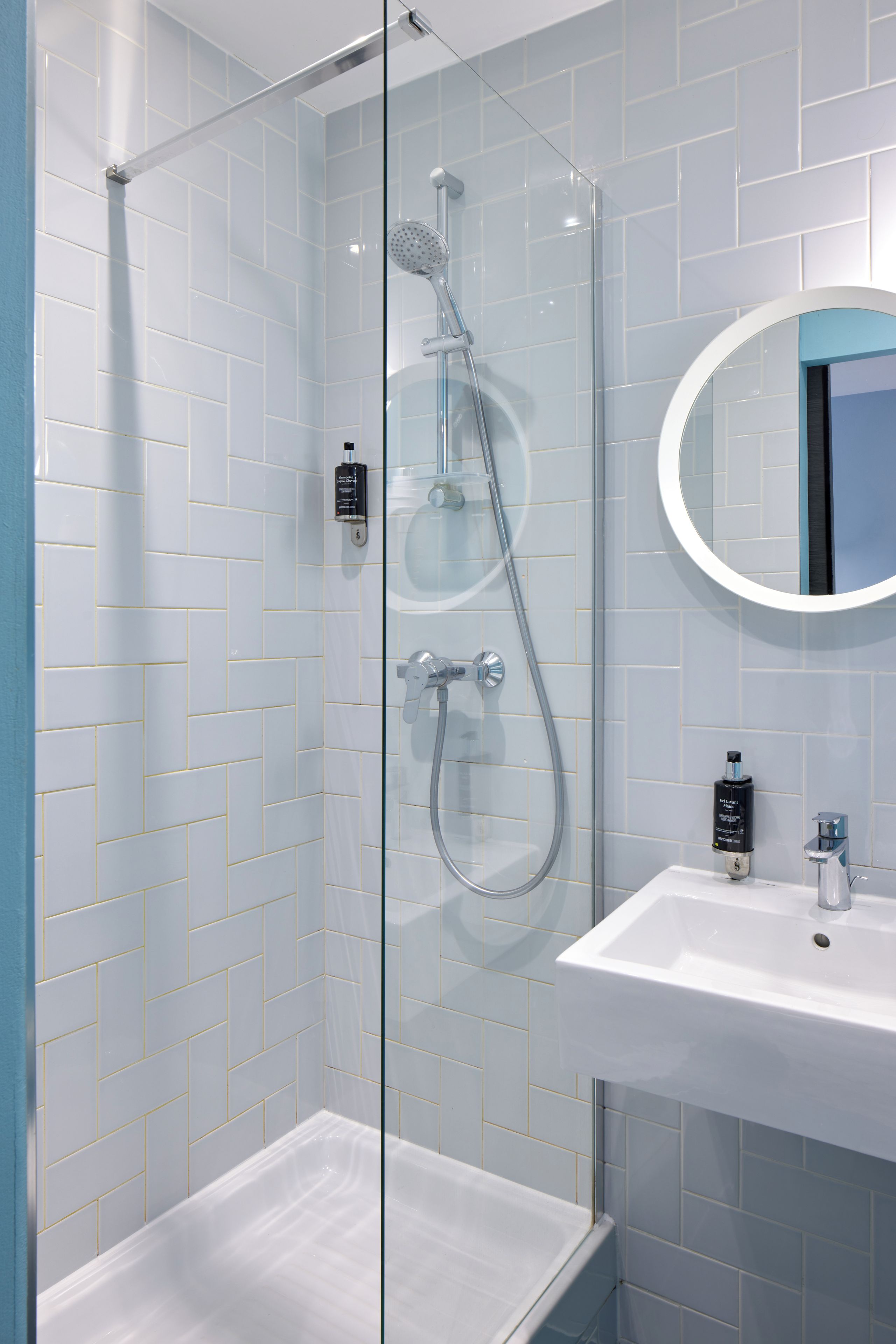 Un baño moderno con ducha envuelta en vidrio, un lavamanos blanco y un espejo redondo.